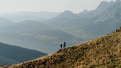 Zwei Personen in sommerlicher Naturkulisse vor Wiese, Wald und Bergen