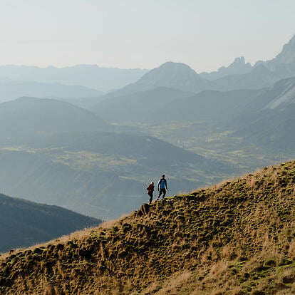 Zwei Personen in sommerlicher Naturkulisse vor Wiese, Wald und Bergen