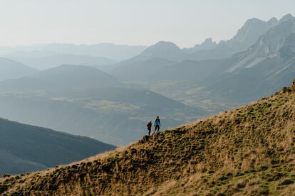 Zwei Personen in sommerlicher Naturkulisse vor Wiese, Wald und Bergen