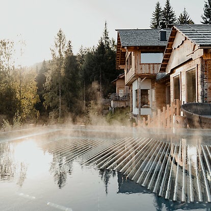 Beheizter Pool im Naturwellnessbereich mit Außenansicht der Holz-Ruhehäuser bei Morgenstimmung