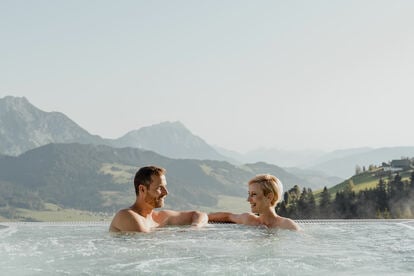 Paar unterhält sich im Luxury Infinity Pool des Natur- und Wellnesshotel Höflehner. Im Hintergrund erkennt man die Ennstaler Bergwelt.