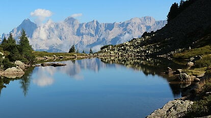 Ruhiger Bergsee spiegelt die Felsen und Wälder der alpinen Landschaft.
