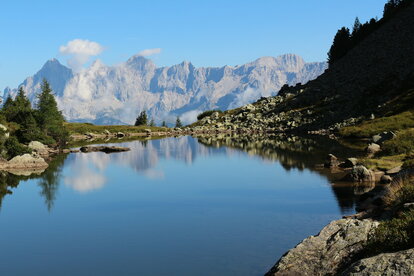 Ruhiger Bergsee spiegelt die Felsen und Wälder der alpinen Landschaft.