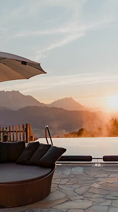 Pool im Vordergrund bei Sonnenaufgang und Blick auf das Ennstal und die Bergew.